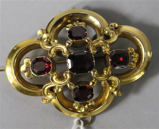 A Victorian metal open work scroll brooch set with five facet cut garnets, 63mm.